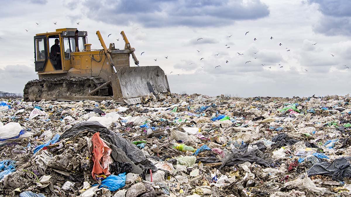 Huge landfill full of waste with a track-type tractor. Birds circling above.