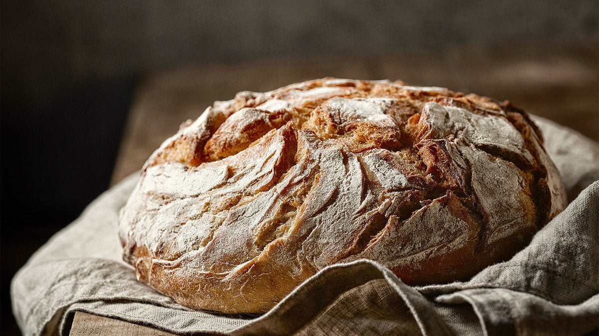 A loaf of bread on a kitchen towel on top of a butcher board. Question: Can dogs eat bread?