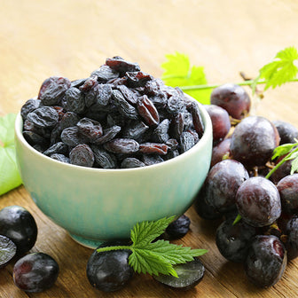 Raisins in a bowl with fresh grapes on a table. Caution: Neither grapes nor raisins should be given to dogs. They are toxic to canines.